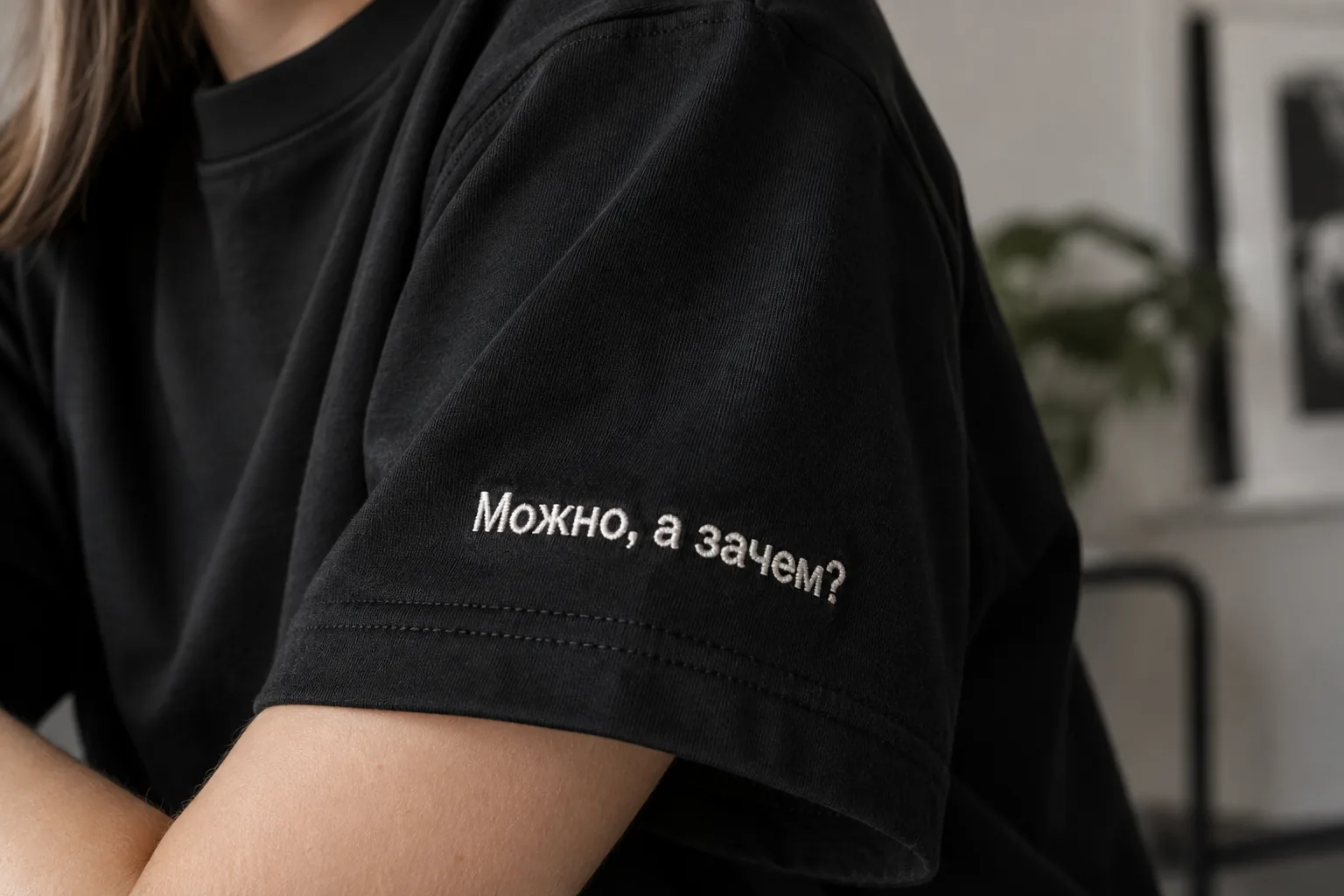 Крупный план рукава чёрной футболки с небольшой светлой вышитой фразой «Можно, а зачем?»